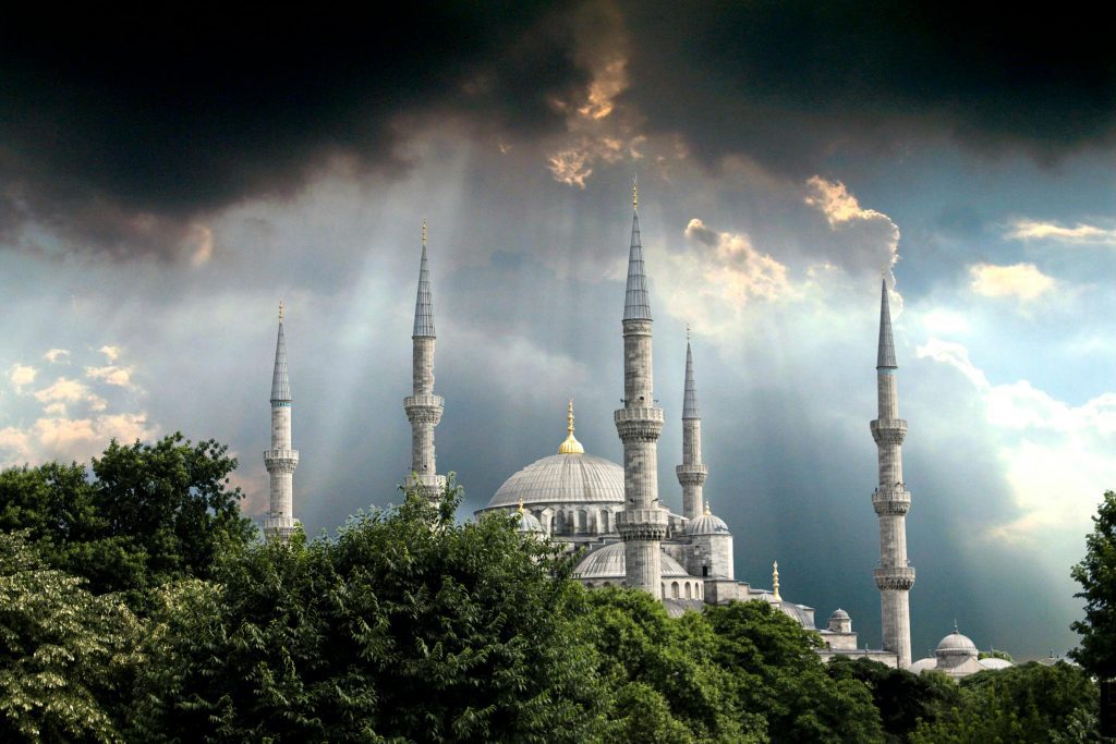 The Blue Mosque in Istanbul during a dramatic sky with sun rays piercing through dark clouds.