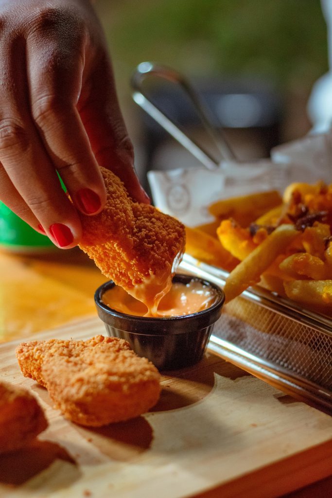 Close-up of chicken nuggets and fries being dipped in sauce. Unhealthy fast food snack.
