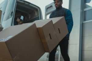 Delivery man carrying cardboard boxes from a van outside a modern building.