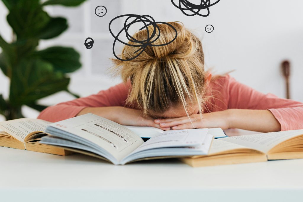 Young woman asleep over books at desk, conveying stress and mental overload. sales training